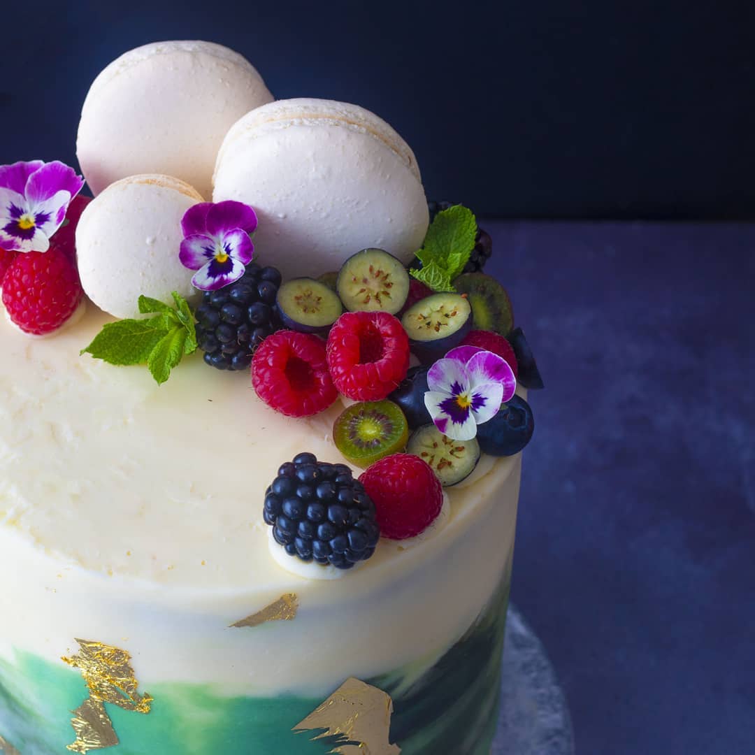 White blue cake decorated with berries and macarons